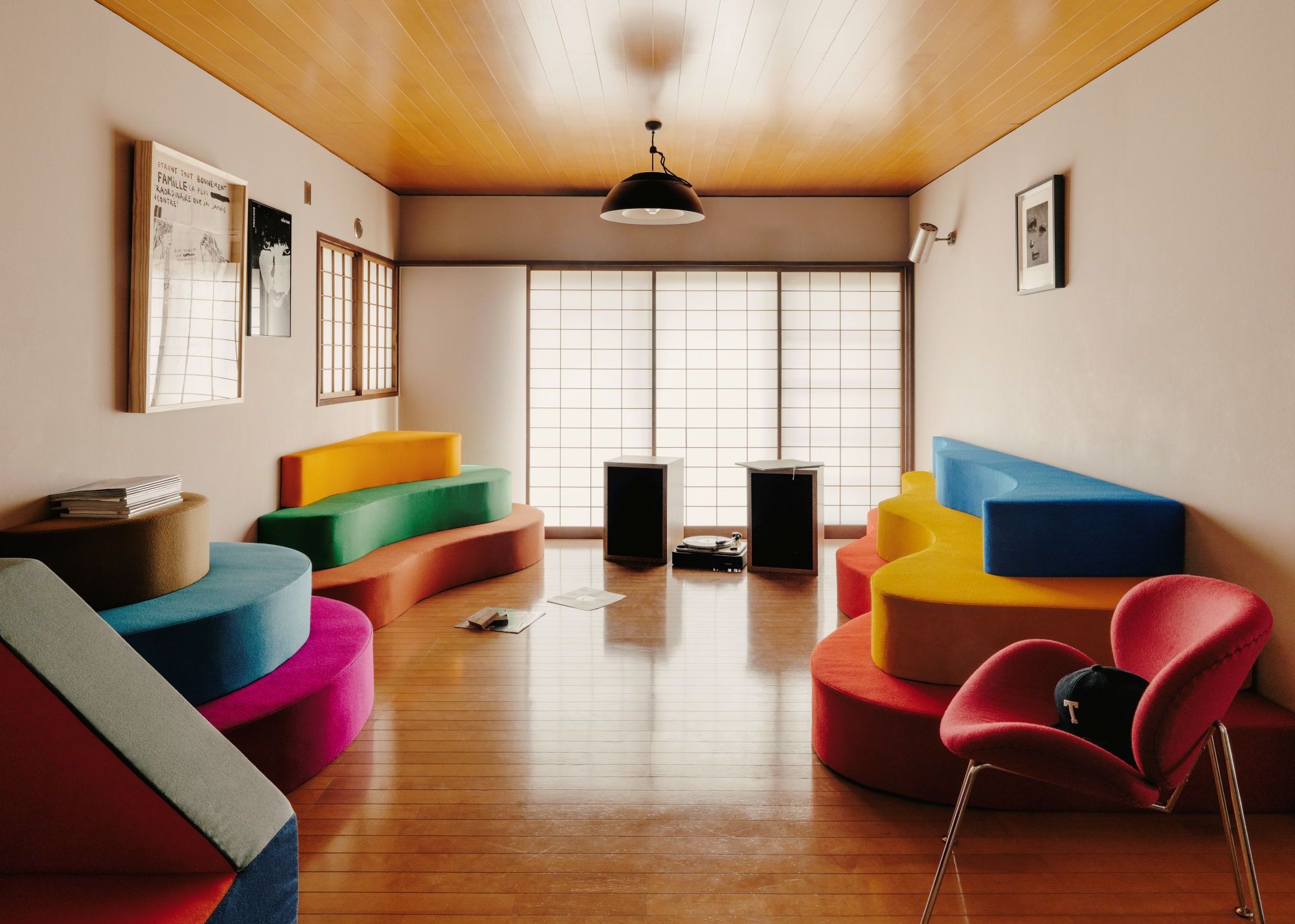A colorful Japanese living room with multicolored wavy and curved seating that is almost like furniture, shoji screens, and neutral walls with a wood paneled ceiling