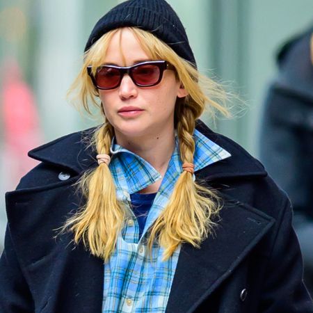 Jennifer Lawrence in New York City wearing a long navy-blue coat with black trousers, sunglasses, flat shoes, and a plaid shirt. 