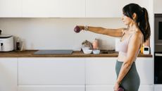 Woman doing lateral raises as part of a dumbbell workout at home in kitchen