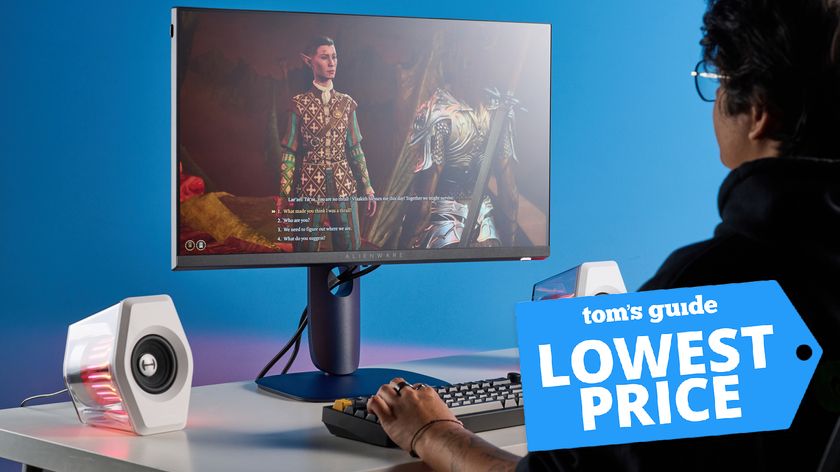 Alienware AW2525HM monitor on table with speakers and person using keyboard with Tom&#039;s Guide Lowest Price badge