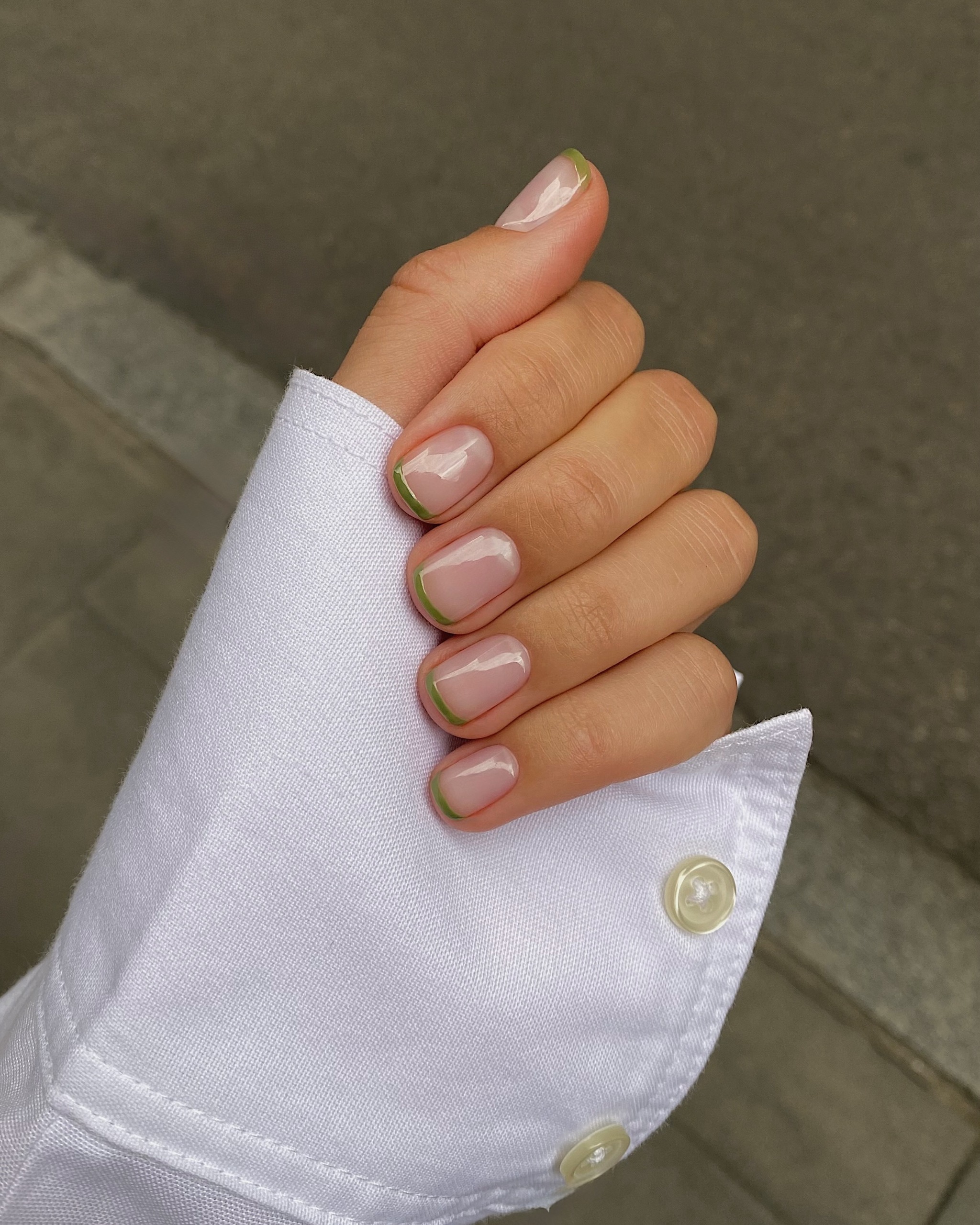 short nails with pale green French tips and a thin gold accent, hand tucked into a white shirt sleeve