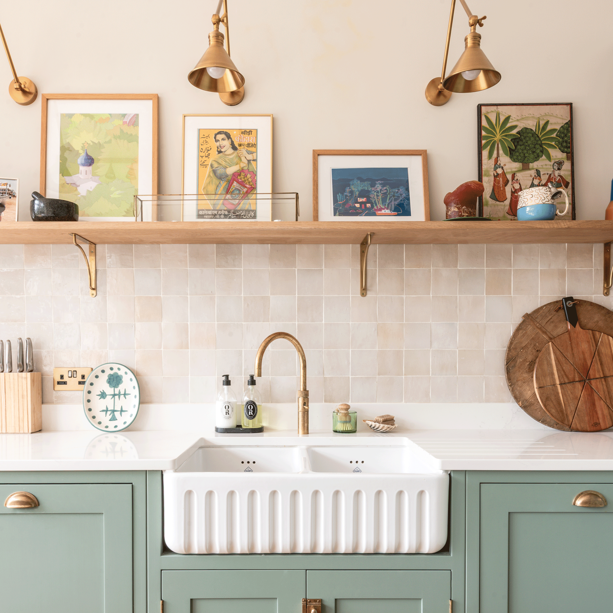 a kitchen with sage green cabinets and a fluted double Belfast sink with brass hot water tap, tiled splashback and open shelving