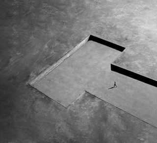 Aerial view of a person walking near a large geometric shadow on a textured surface