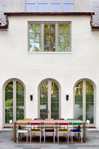 back of white rendered house with arched windows and long outside table with multicolored chairs