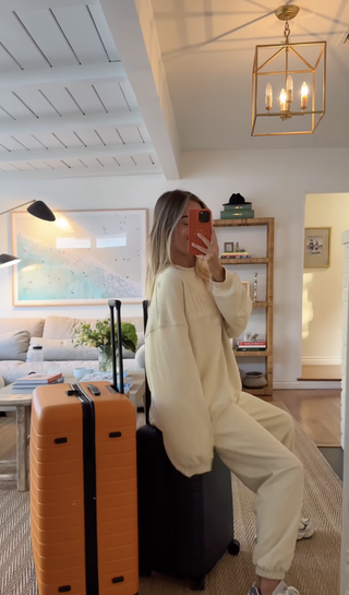 Daily Drills co-founder Mary Ralph Lawson sitting on top of luggage wearing white sweat set.