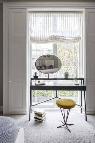 black dressing table in front of window, bed in foreground, window blind