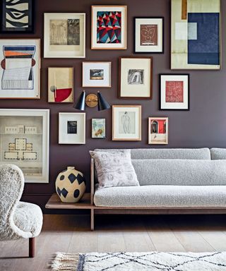 Living room with a sofa and chair, carpet on wood floorboards and a gallery wall full of artworks.