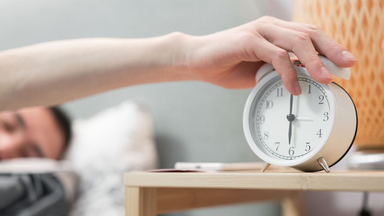 person in bed, reaching to switch off their alarm clock