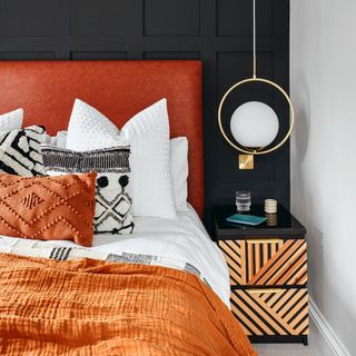 Black panelled bedroom wall, orange headboard, white bedding with orange cushion and throw, black patterned bedside table
