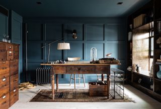 A home office with wall panelling all painted in deep blue hue