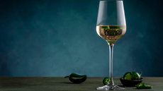 A glass of wine with slices of jalapeno in it, and japapeno peppers next to it. 
