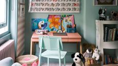 a kids bedroom with a pink desk with artworks on and toys and books around