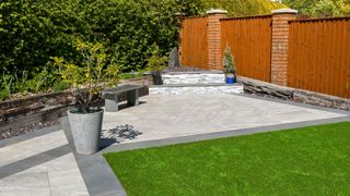 Residential back garden landscaped with light and dark grey porcelain paving slabs and artificial grass