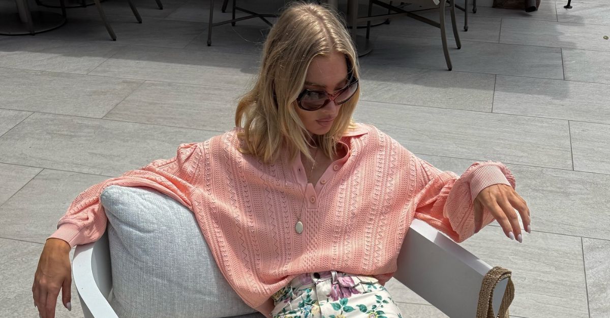 Model @hoskelsa sits on an armchair wearing floral high-waisted jeans with suede sandals and a peach lightweight knit.