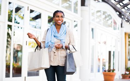 Beautiful Girl in her 20s loves shopping. Young woman is of Black descent. African American woman is walking in a mall and holding three shopping bags. Her hair is in braids. Woman is dresses