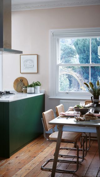 a peninsula in a green kitchen with white marble countertops, a dining table at one end