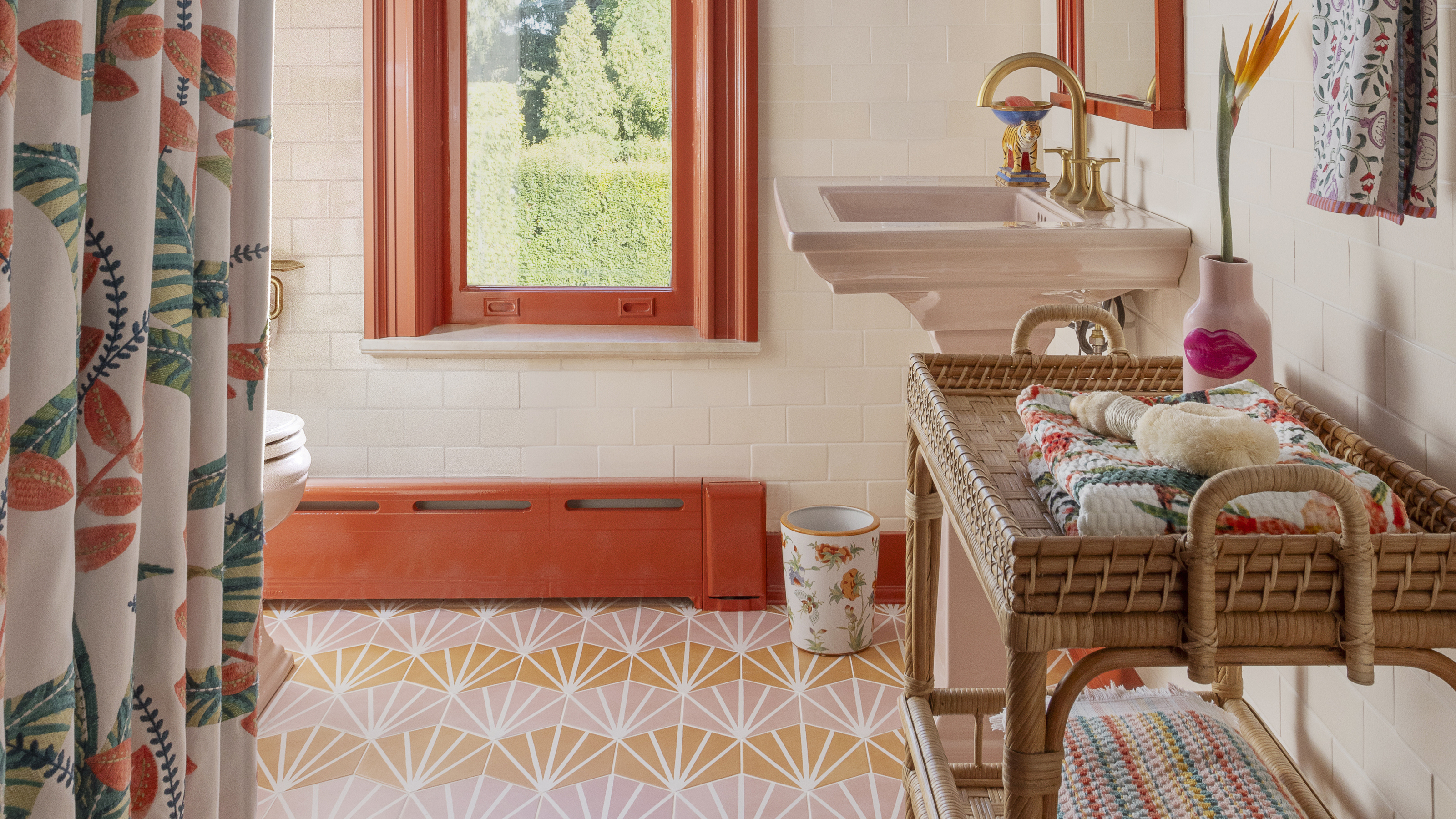 A colorful bathroom with a patterned tile floor, red trim accent, and a rattan rolling cart in the foreground holding towels
