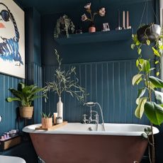 Bathroom with teal painted wall panelling and painted roll-top bath surrounded by houseplants
