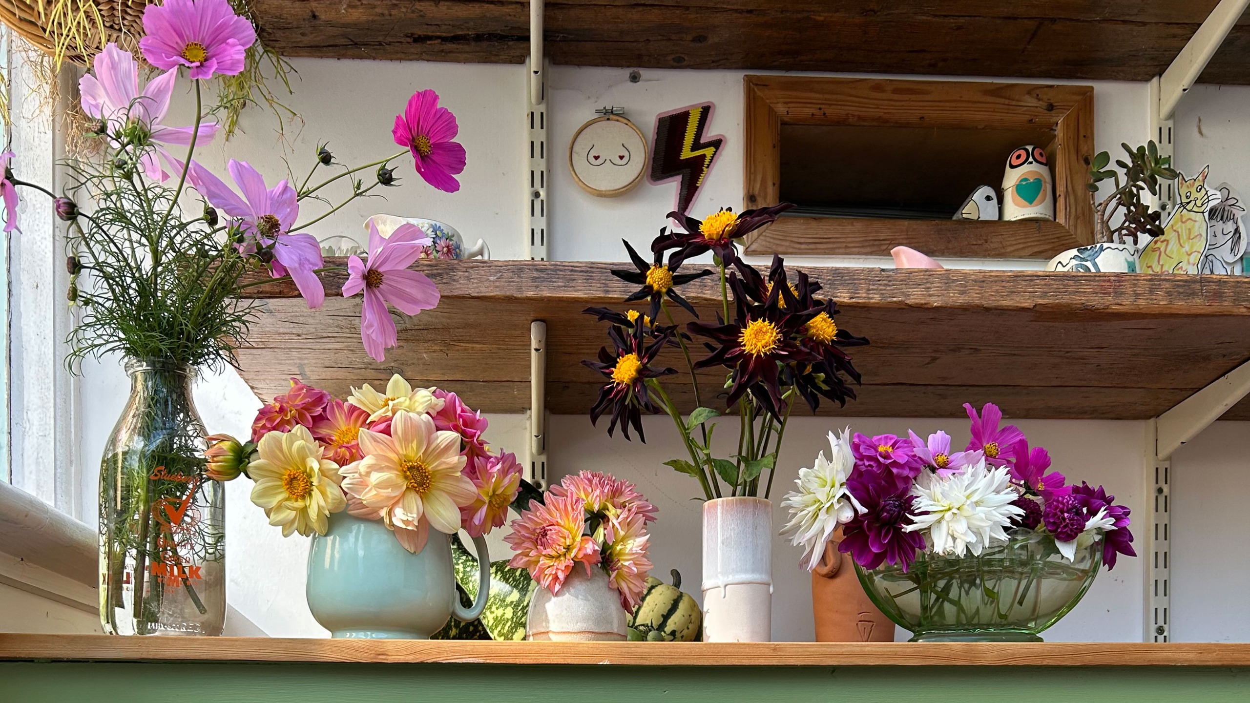 Vases and bowls full of flowers on shelf 