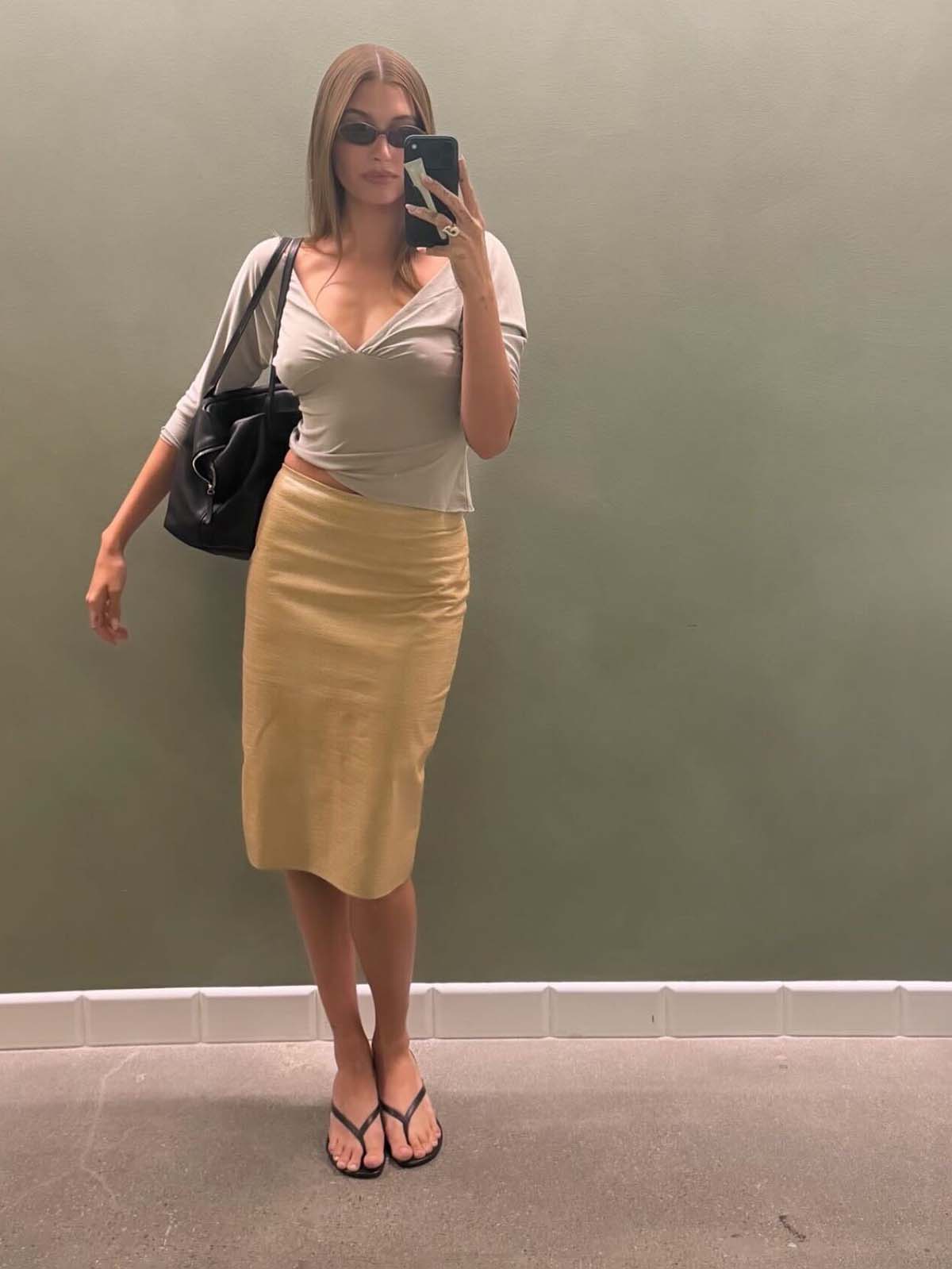 Hailey Bieber taking a selfie wearing a leather pencil skirt, heeled flip-flops, and a With Jean top.