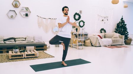 Man performing yoga at home with holiday decorations in the background