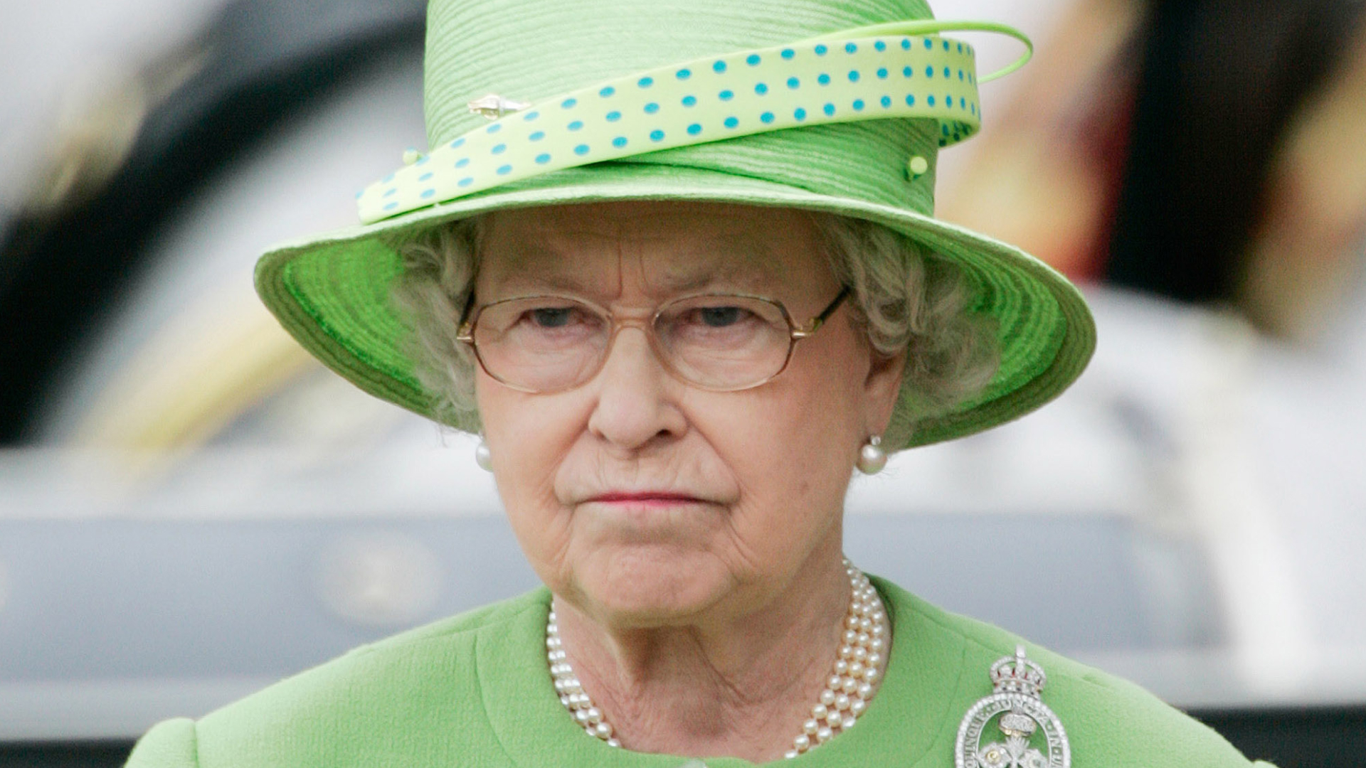 Queen Elizabeth II purses her mouth and looks annoyed while wearing a lime green coat dress and a matching hat in 2007