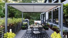 An outdoor deck with a pergola, a dining table, and an outdoor kitchen surrounding by potted shrubs and plants