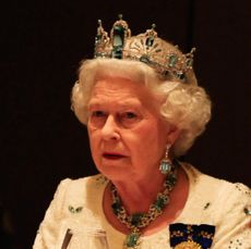 Queen Elizabeth wearing a tiara, white dress and diamond necklace sitting at a table in the dark