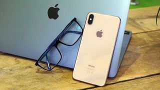 A pair of glasses next to an iPhone, resting on a MacBook