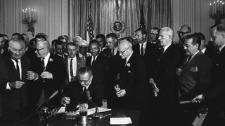 President Lyndon B. Johnson signs the Civil Rights Act, with Martin Luther King Jr. standing behind him, in 1964.