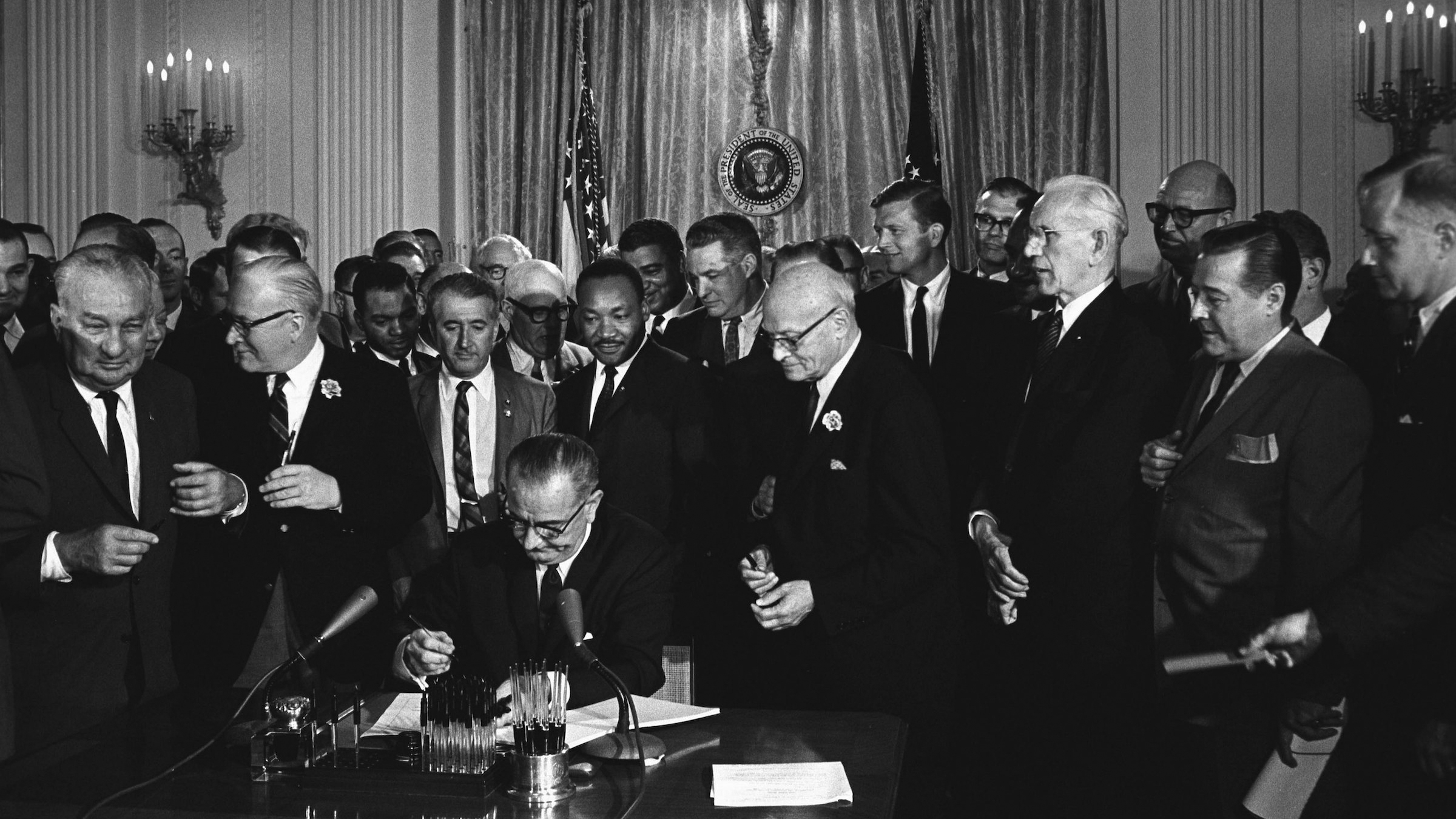 Präsident Lyndon B. Johnson unterzeichnet 1964 den Civil Rights Act, hinter dem Martin Luther King Jr. steht.
