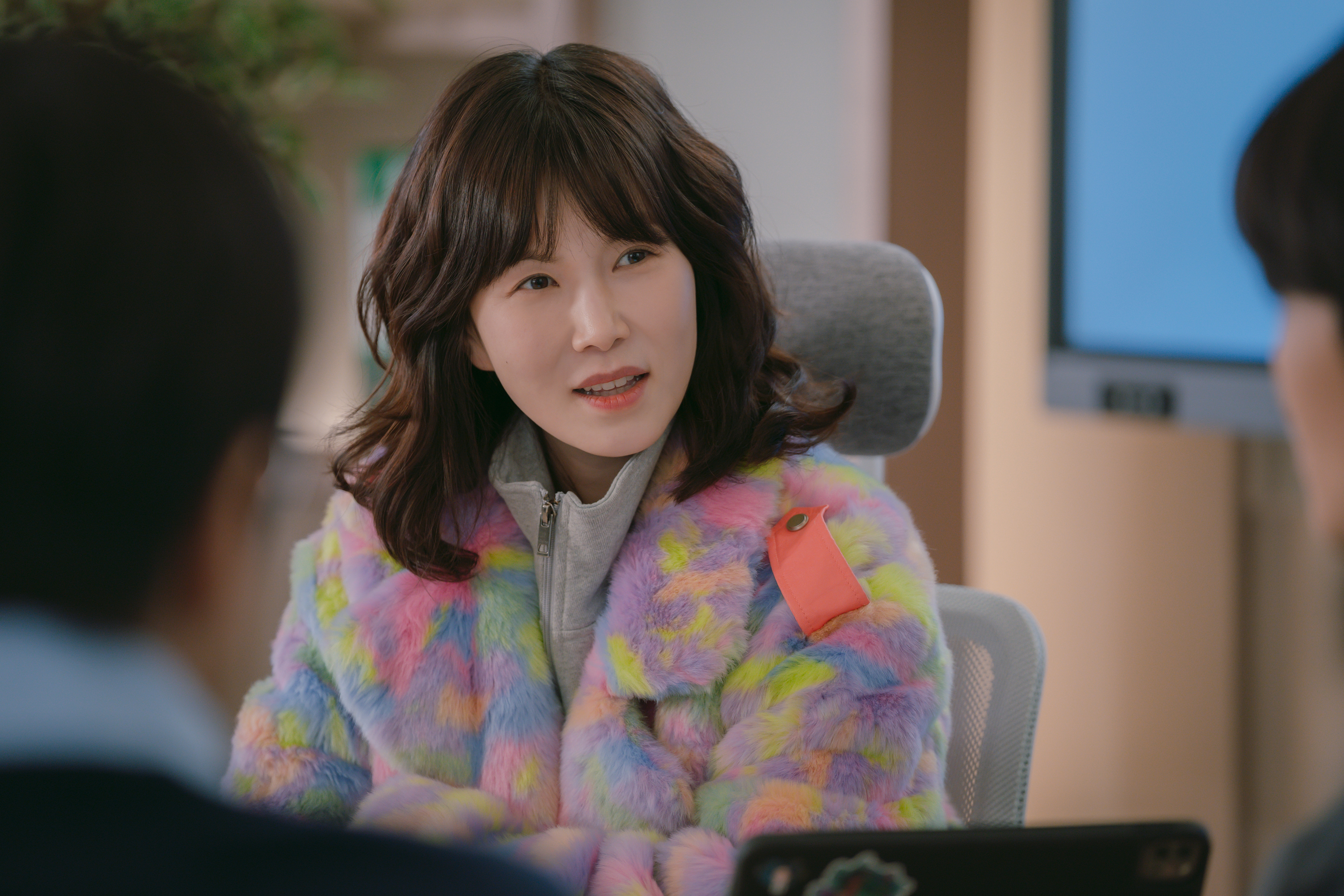 A woman (Gong Min-jeung as Yun Song) wears a fluffy pastel sweater while sitting in an office conference room, in the Netflix K-drama 'Boyfriend on Demand.'