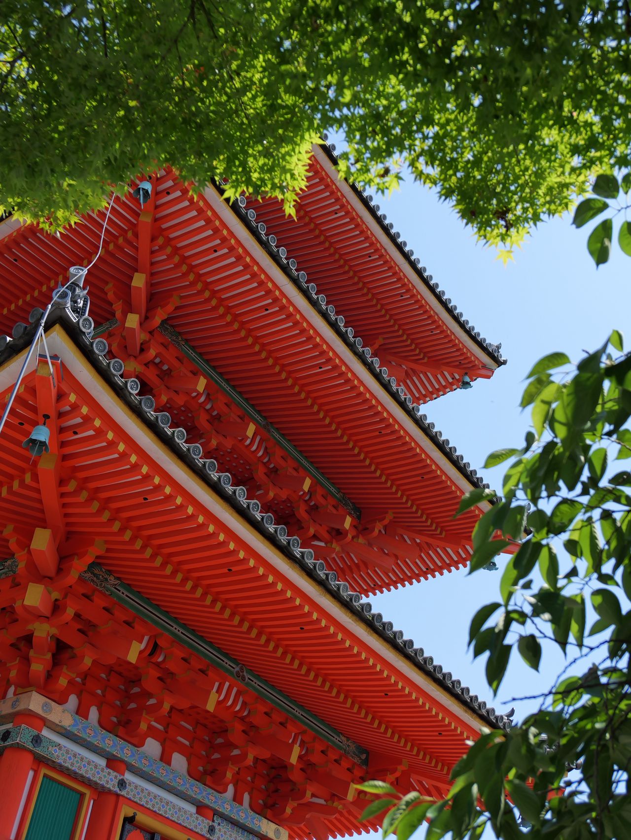 Red pagoda roof framed by green leaves against a blue sky.