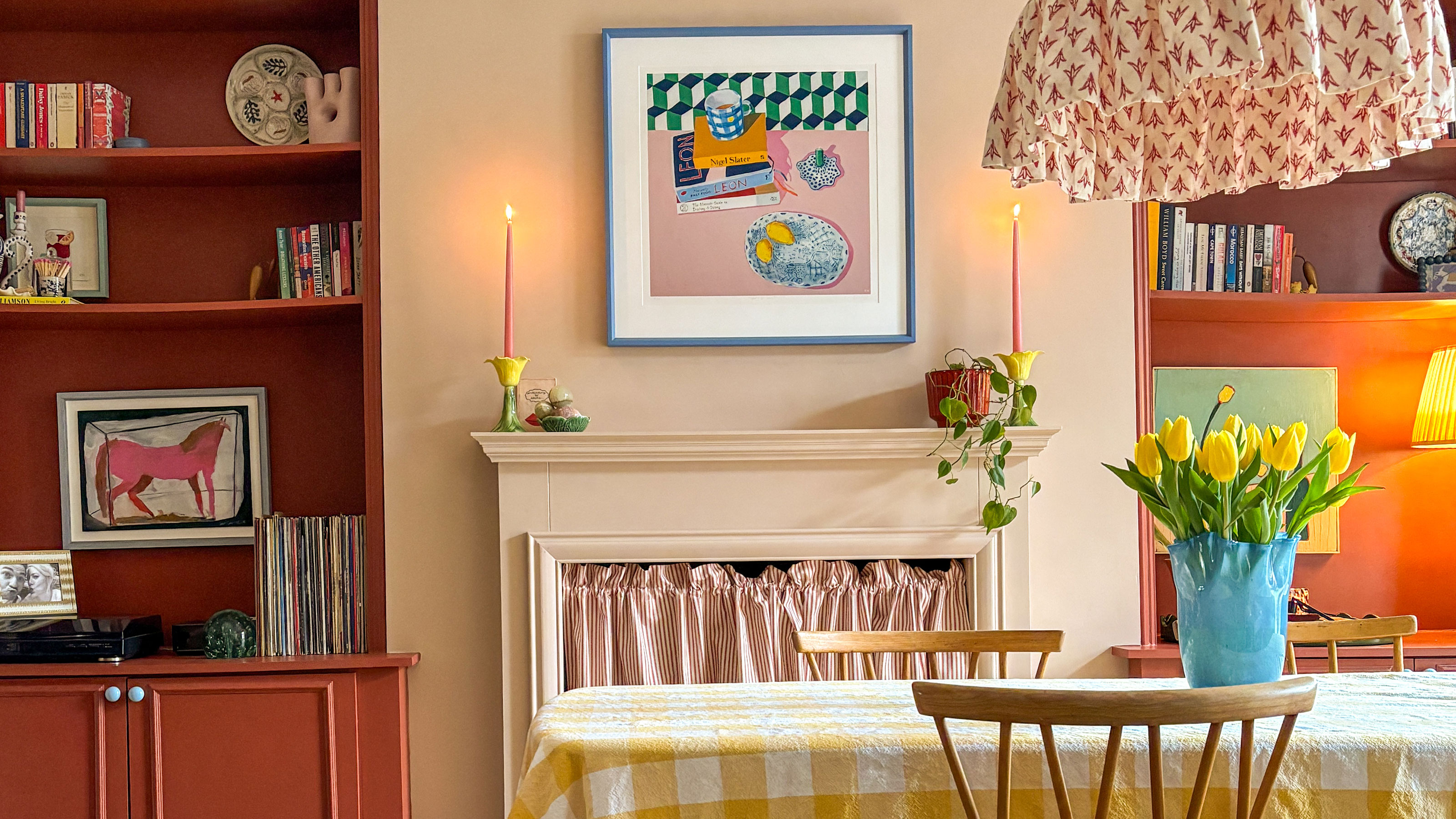 Dining room with yellow and white gingham tablecloth, cream-peach walls and terracotta built-in shelving on either side of mantlepiece area