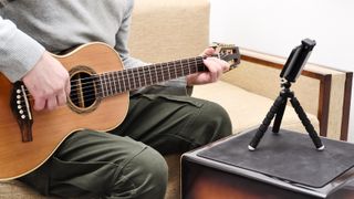 Man plays travel guitar with a mobile phone on a tripod