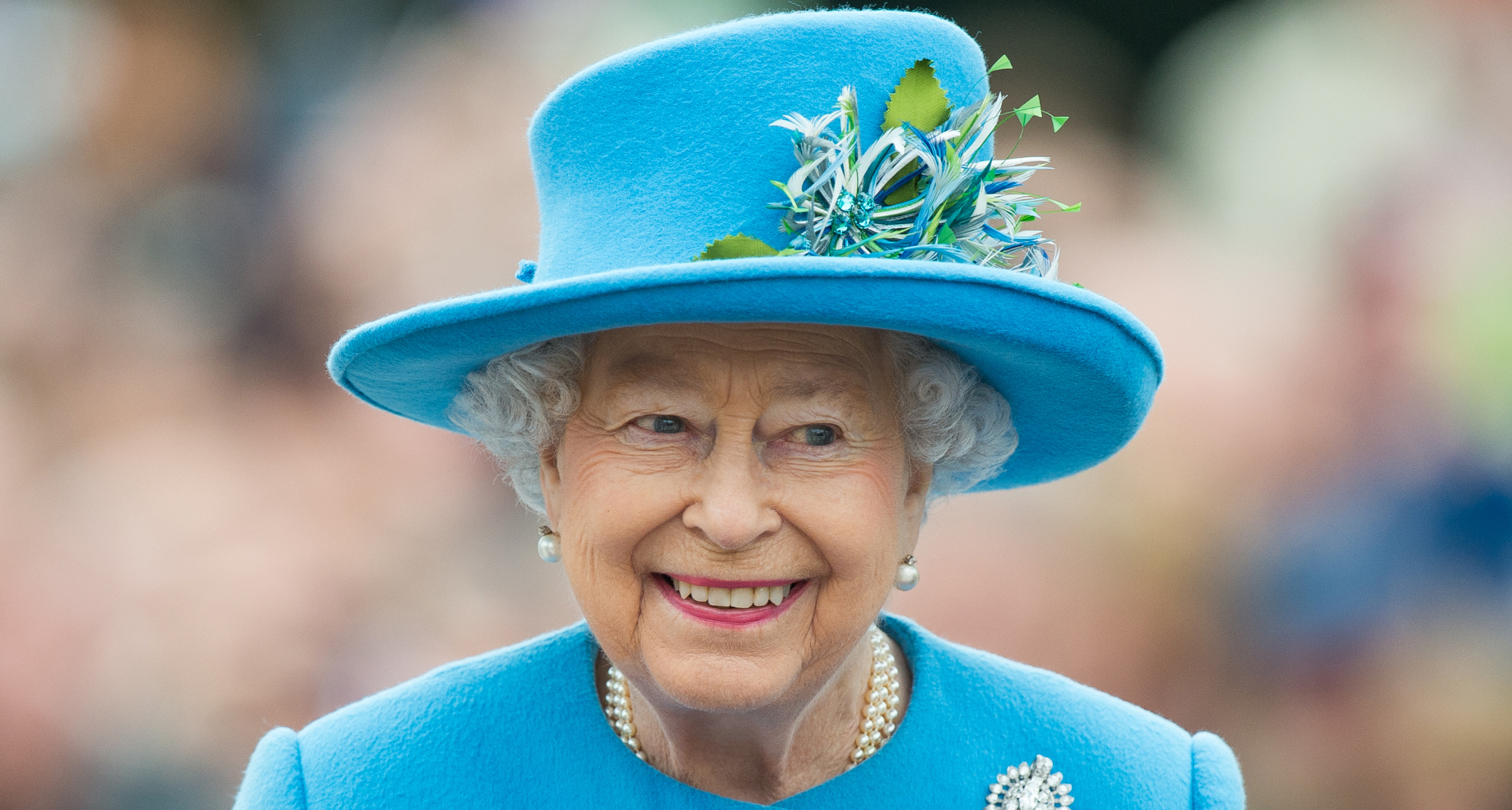 Queen Elizabeth smiling in a blue hat and coat