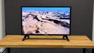 RCA Roku TV 24-inch (RK24HF1) small TV on wooden TV stand showing sand dunes on screen
