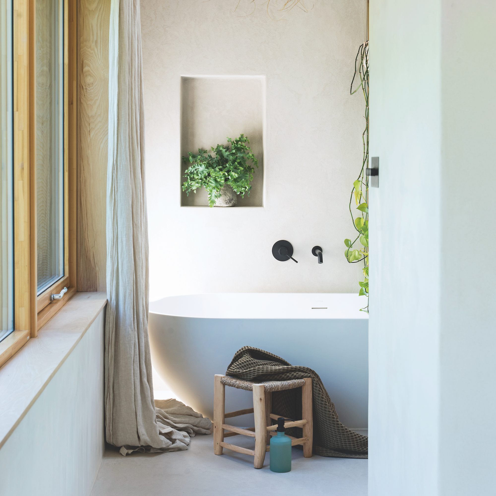 contemporary bathroom with freestanding oval white bath, stool next to bath and small recess with a pot plant