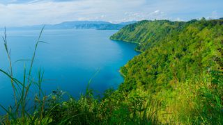 view of Lake Toba with hills covered in gree foliage to the right and islands in the background
