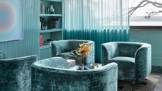 Image of a living room that is color-drenched in a teal-cyan color. The walls are painted in cyan, there are cyan curtains, and the four accent chairs are in a darker teal color. 