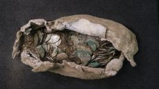 An excavated cloth and lead pouch full of silver coins dating to between 1042 and 1044. The pouch sits on a black background.