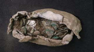 An excavated cloth and lead pouch full of silver coins dating to between 1042 and 1044. The pouch sits on a black background.