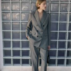 A woman leaning against a tiled wall wearing a grey women's suit