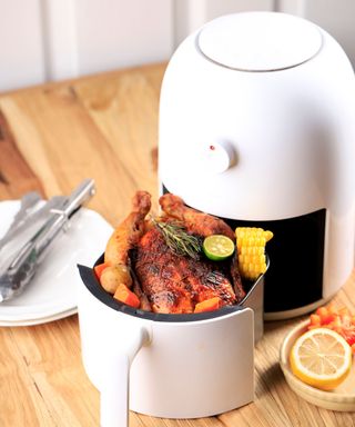 A white air fryer on a kitchen counter with a roast chicken inside
