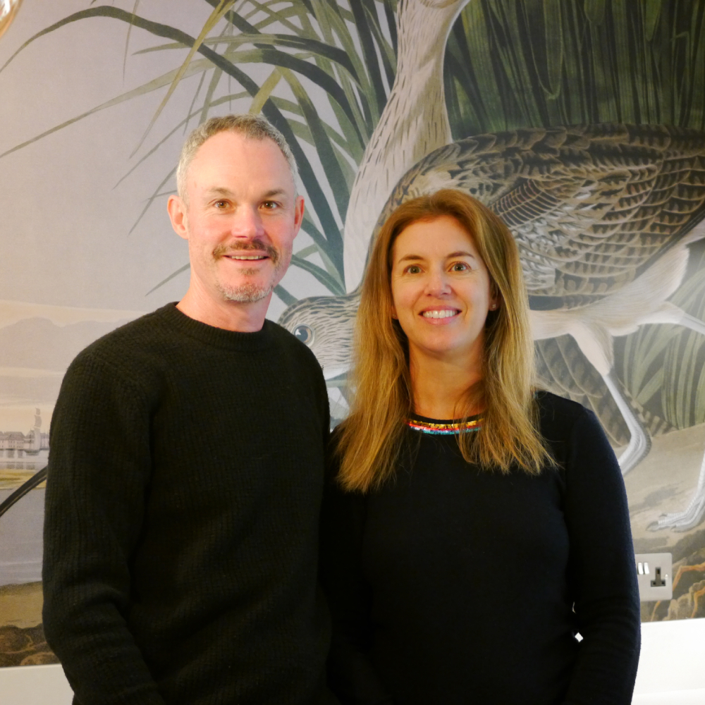male and female stood against large wall panel featuring a bird