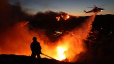 A firefighter responds to the Palisades Fire as a helicopter drops water in Los Angeles on Jan. 7, 2025.