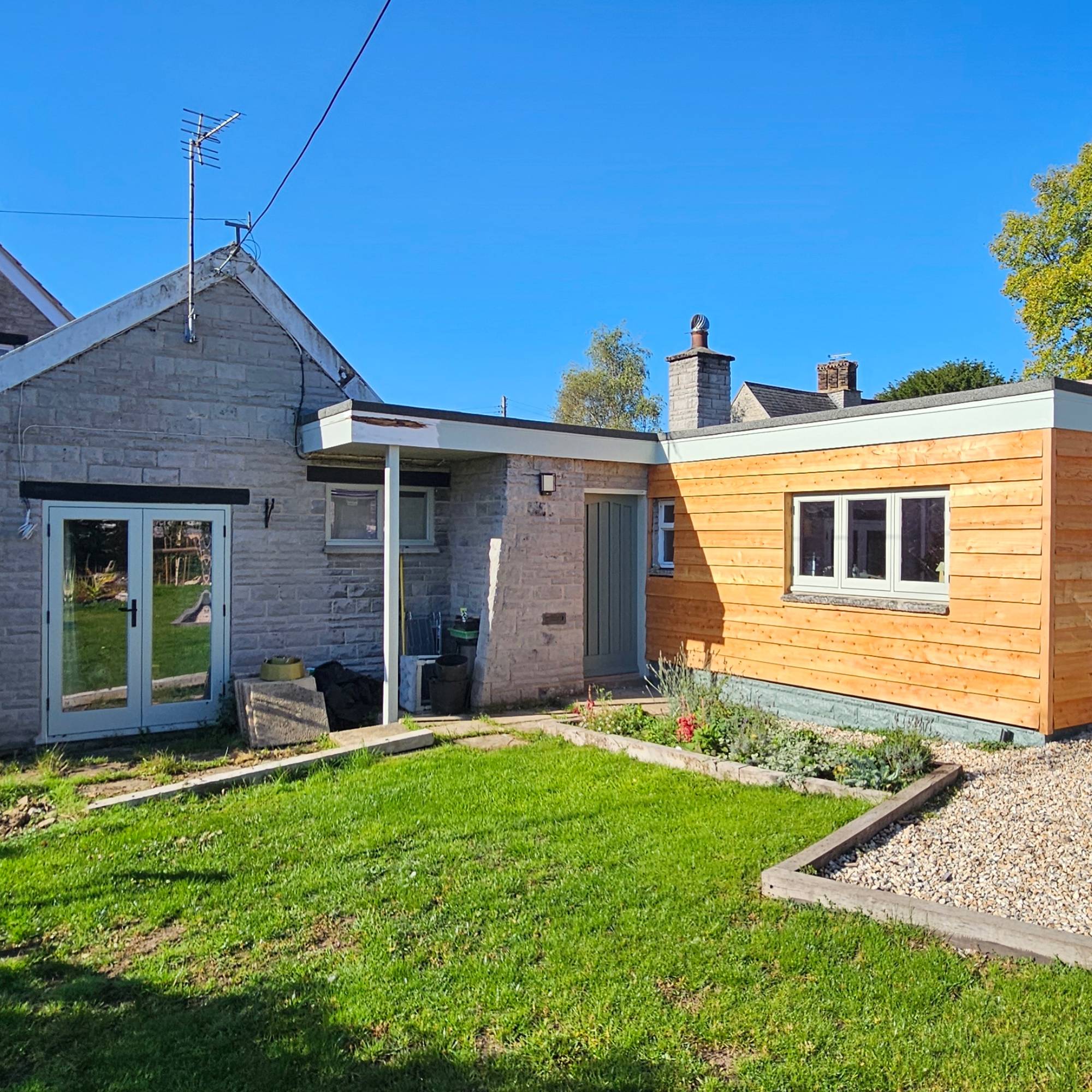 Light blue windows in stone and wood extension with lawn