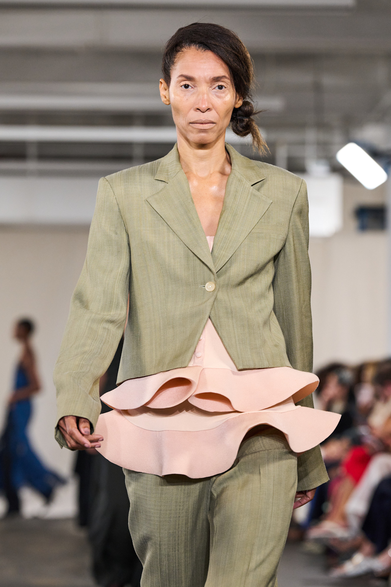 a model on the runway in a low side bun and green suit