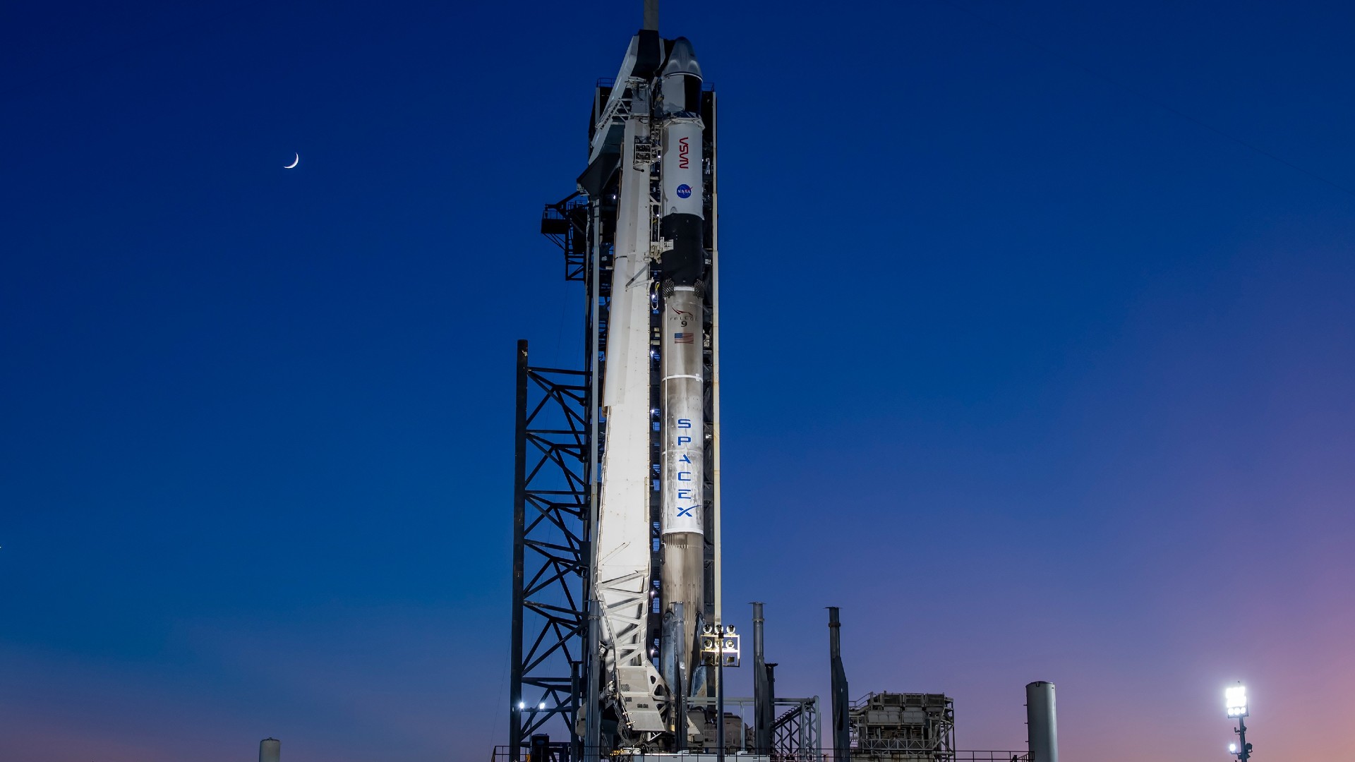 a white rocket upright on a launch pad at sunset