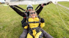 An older woman and her tandem parachuting instructor celebrate a safe landing.